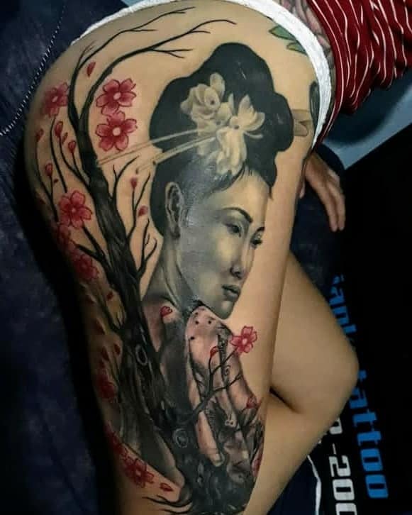 Black and gray thigh tattoo of a Geisha emerging from a cherry blossom tree, with red flowers accenting the design and intricate shading details.