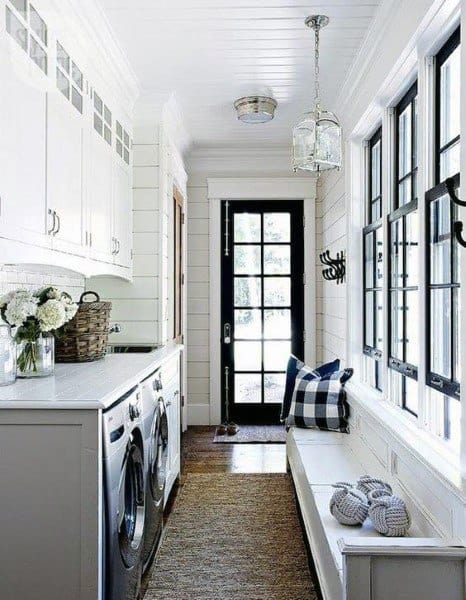 Farmhouse-style laundry room with white cabinets, black windows, and a cozy bench with cushions.