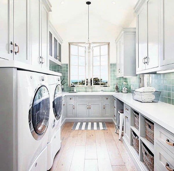 Bright laundry room with gray cabinets, green tile backsplash, and large windows with natural light.