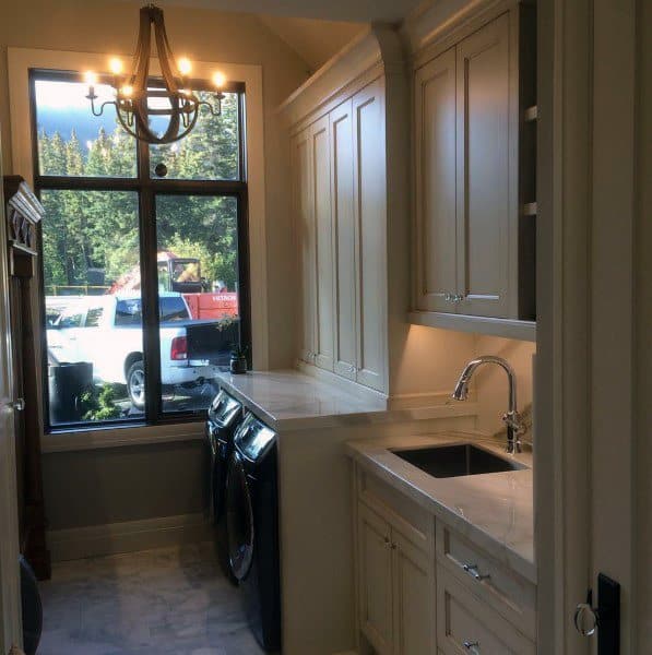 Cozy laundry room with beige cabinets, black appliances, a chandelier, and a large window view.