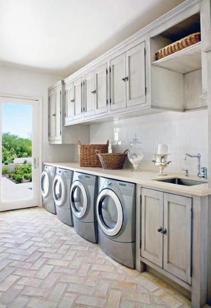 Laundry room with rustic white cabinets, stainless steel appliances, and herringbone tile flooring.