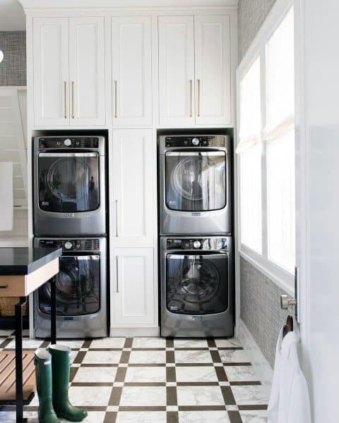 Laundry room with stacked stainless steel appliances, white cabinets, and checkered tile flooring.