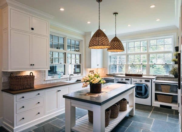 Bright laundry room with white cabinets, slate flooring, woven pendant lights, and large windows.