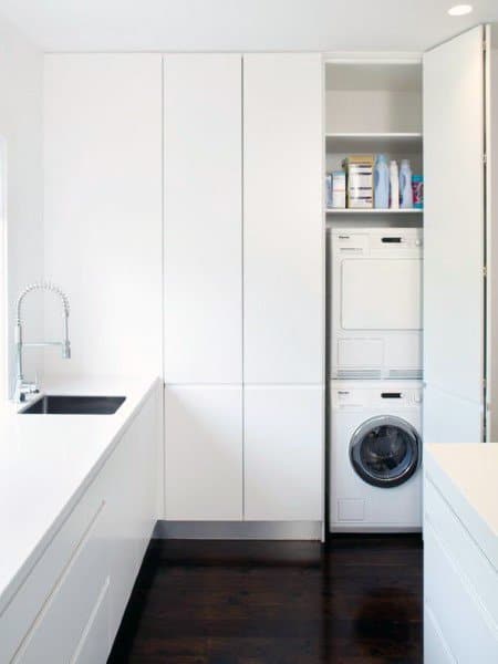 Minimalist laundry room with white cabinets, stacked appliances, and sleek dark flooring.