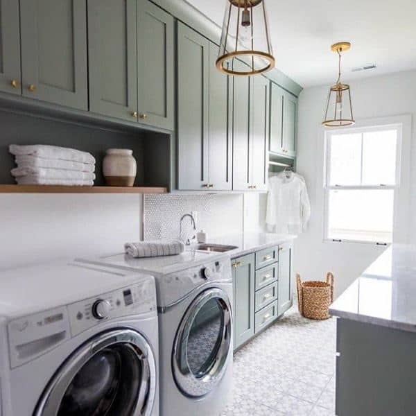 Laundry room with green cabinets, white appliances, brass accents, and patterned tile flooring.