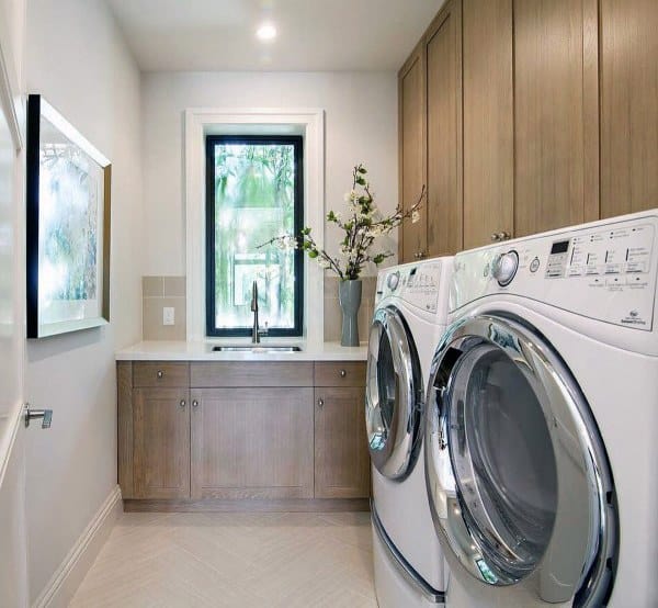 Laundry room with wood cabinets, white appliances, a central sink, and a narrow window view.