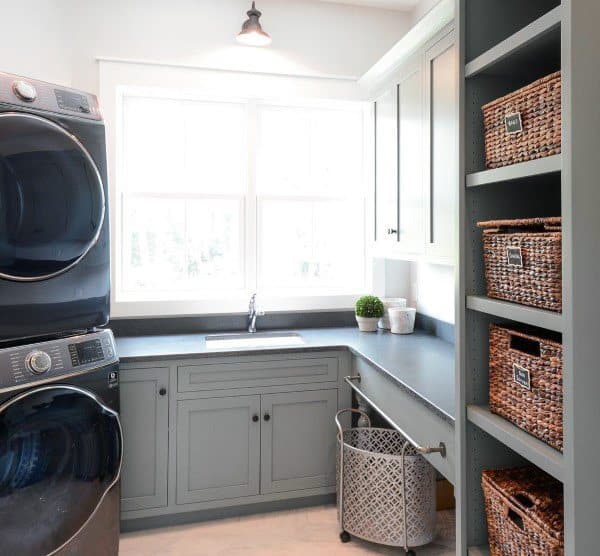 Laundry room with gray cabinets, stacked black appliances, open shelving, and wicker storage baskets.