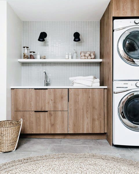 Modern laundry room with wood cabinets, mosaic tile backsplash, and stacked washer-dryer units.
