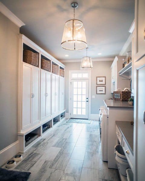 Spacious laundry room with white cabinets, tiled flooring, hanging lights, and natural light from a door.