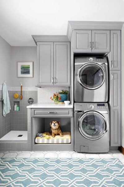 Laundry room with gray cabinets, pet bed nook, stacked appliances, and a tiled washing station.