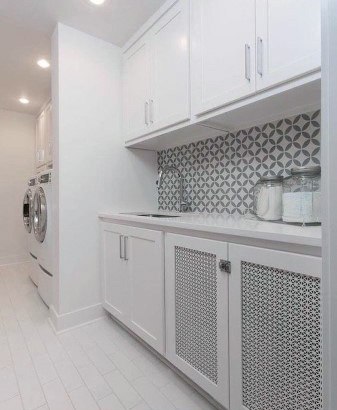 Laundry room with white cabinets, geometric backsplash, and modern washer-dryer units.