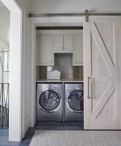 Laundry nook with stainless steel appliances, white cabinets, and a sliding barn door.