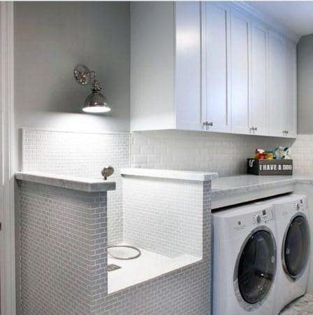 Laundry room with white cabinets, tiled pet washing station, and modern washer-dryer units.