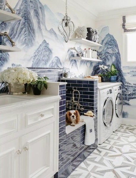 Laundry room with scenic wallpaper, pet washing station, white cabinets, and patterned tile flooring.