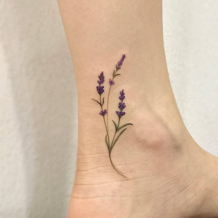 Delicate ankle tattoo of two lilac sprigs with fine-line details and soft purple hues, creating a minimalist and elegant design.