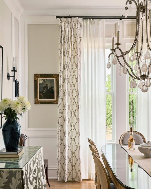 Elegant dining room with layered sheer and patterned curtains, a crystal chandelier, and classic decor.