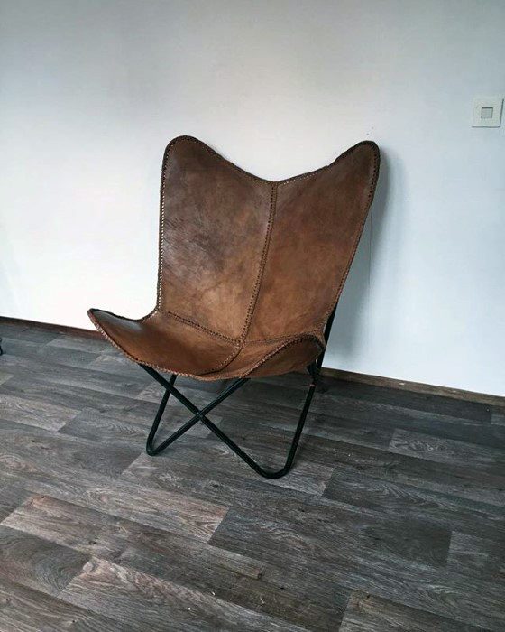 Brown leather butterfly chair on a wooden floor against a plain white wall