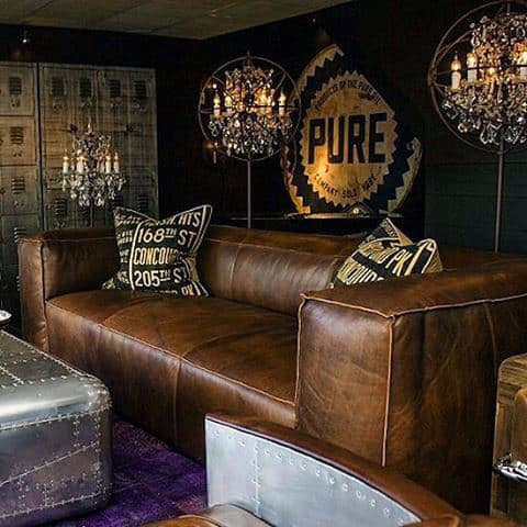 Man cave with a brown leather sofa, industrial decor, and vintage-style chandeliers.