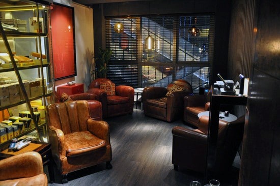 Cozy man cave with leather chairs, warm lighting, and a bookshelf, large window with blinds overlooks the street