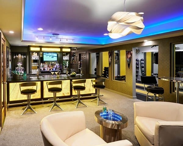 Modern basement bar with cove ceiling lighting, illuminated bar counter, and stylish seating.