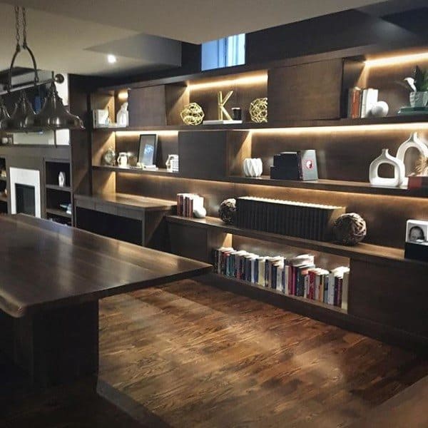 Modern room with wooden shelves, books, and a built-in desk, featuring a wooden table and lit display area