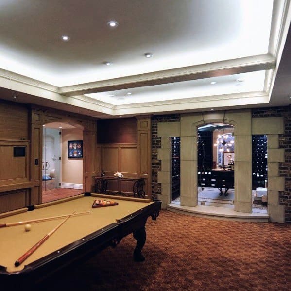 Billiard room with beige pool table tray ceiling recessed lighting and wine cellar entrance.