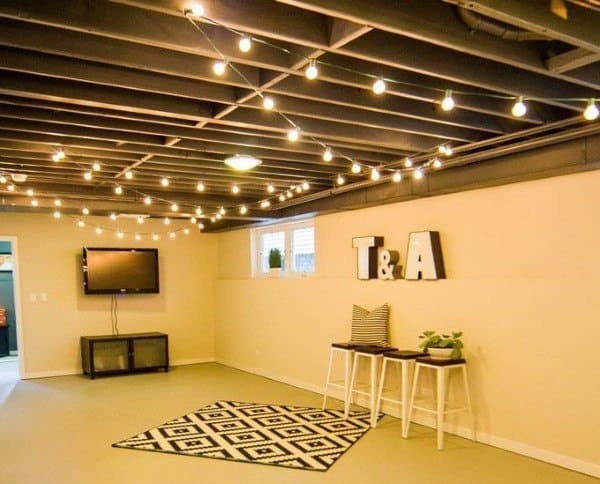 Basement with exposed ceiling and string lights, small TV area, and decorative black-and-white rug.