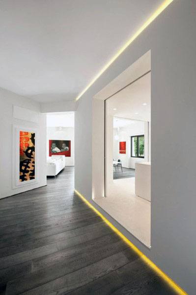 Modern hallway with LED-lit baseboards, white walls, and dark wood flooring.