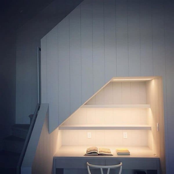 Built-in desk with books, nestled in an illuminated, geometric alcove beside the staircase