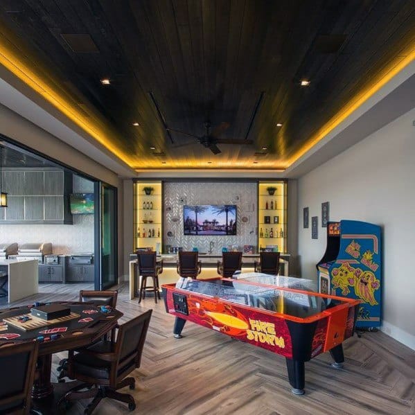 Game room with dark wood ceiling, LED accent lighting, bar area, air hockey table, and arcade games.