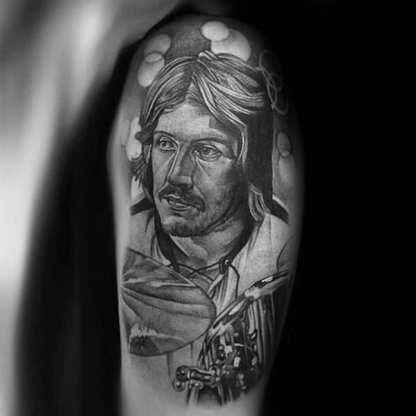 Realistic upper arm tattoo of John Bonham playing drums, with soft shading and the three-ring Led Zeppelin symbol subtly in the background.