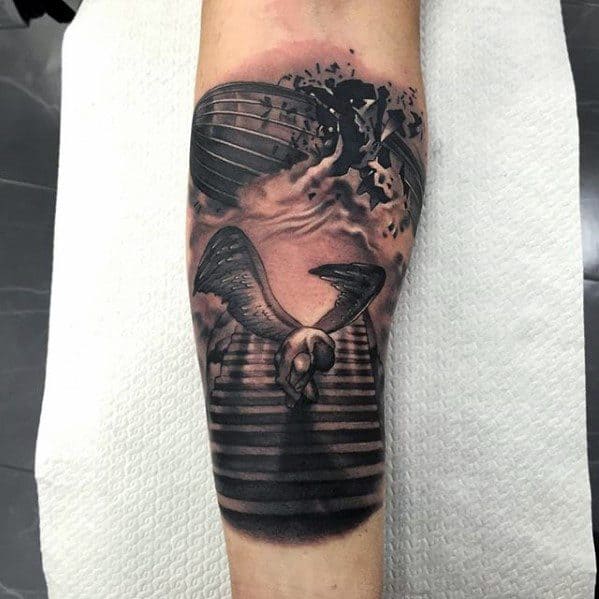Forearm tattoo featuring the Icarus figure at the base of a staircase leading to a dramatic Zeppelin airship explosion in the clouds above.