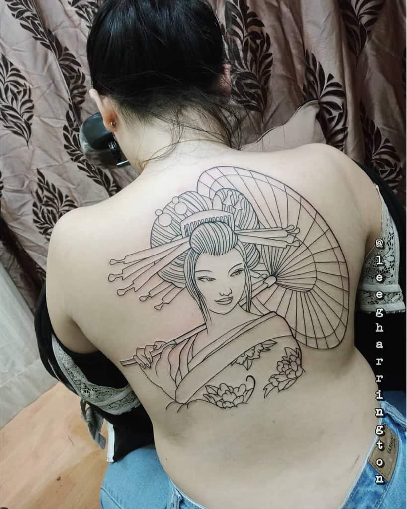 Elegant black linework back tattoo of a Geisha holding a parasol, featuring intricate hair ornaments, floral kimono details, and graceful expression.