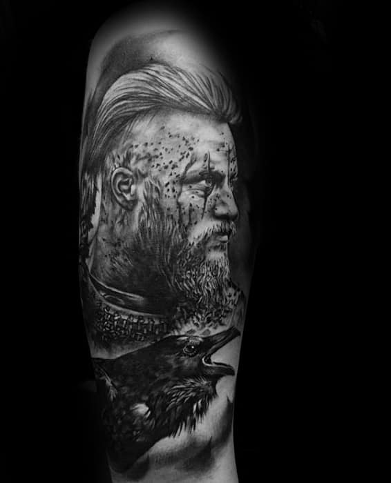 Tattoo of a bearded warrior's face and a crow on a person's forearm