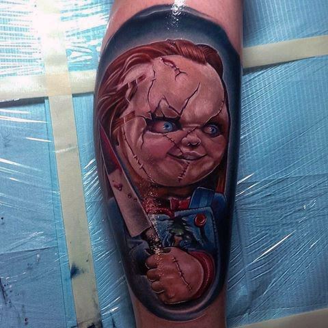 Realistic Chucky tattoo with vivid colors, featuring his stitched face, piercing blue eyes, and a bloodied knife for a striking horror design.