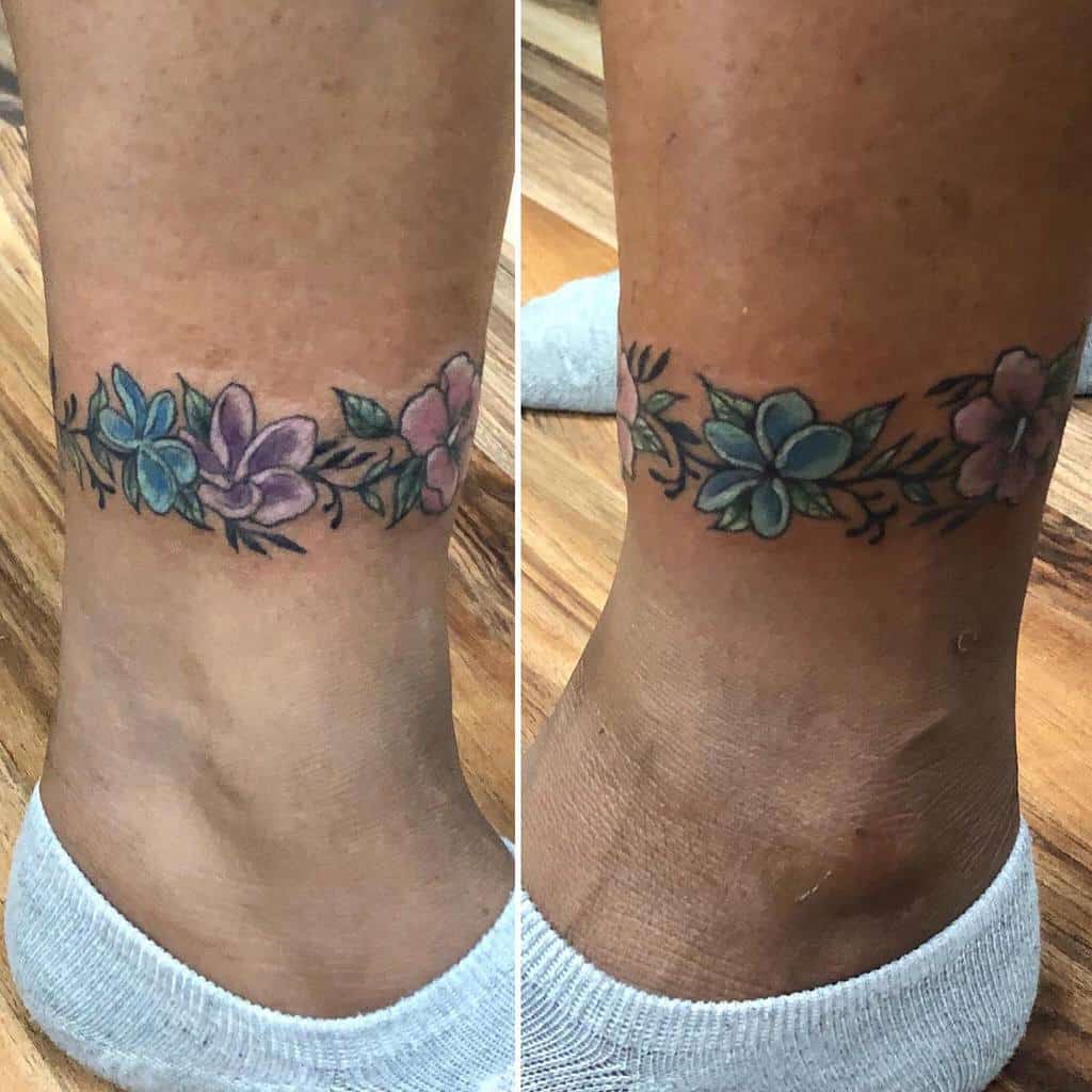 Ankle tattoo of vibrant plumeria flowers with lush green leaves