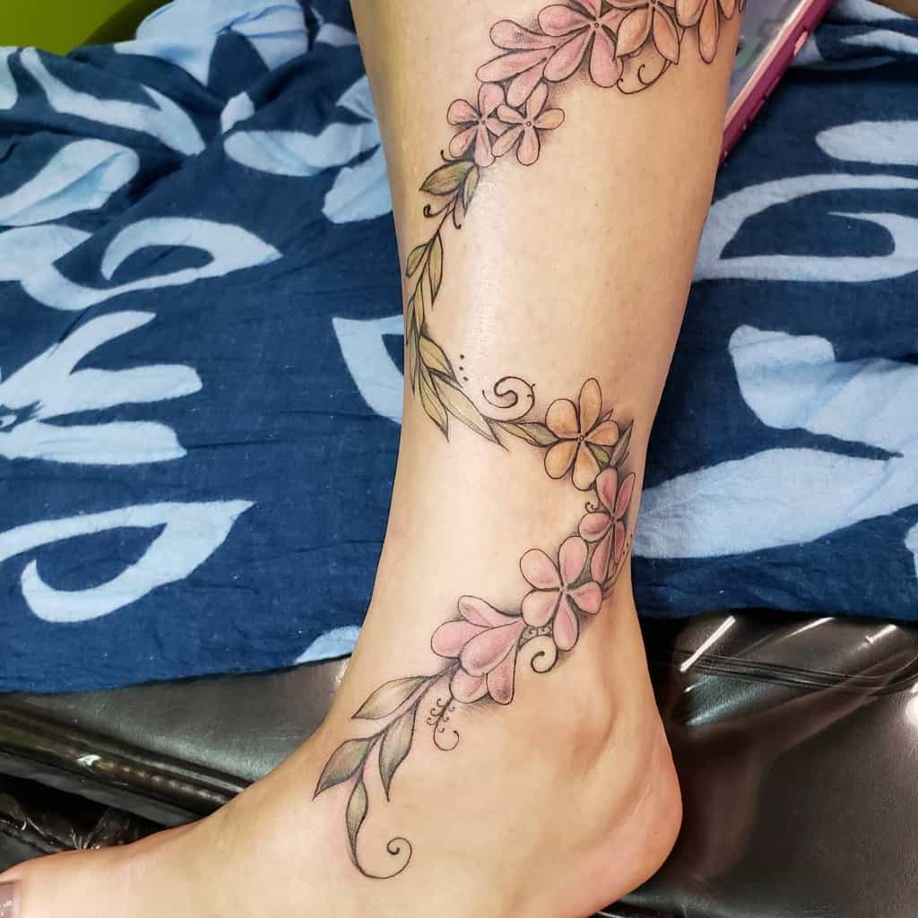 A floral tattoo featuring delicate pink plumeria flowers and lush green leaves adorns the leg