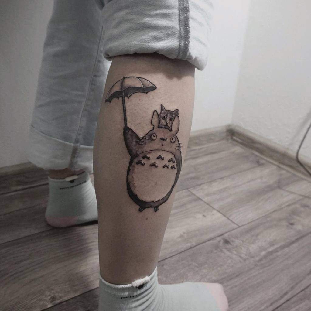 Minimalist Totoro tattoo on the calf, featuring Totoro holding an umbrella with a small companion sitting on his head