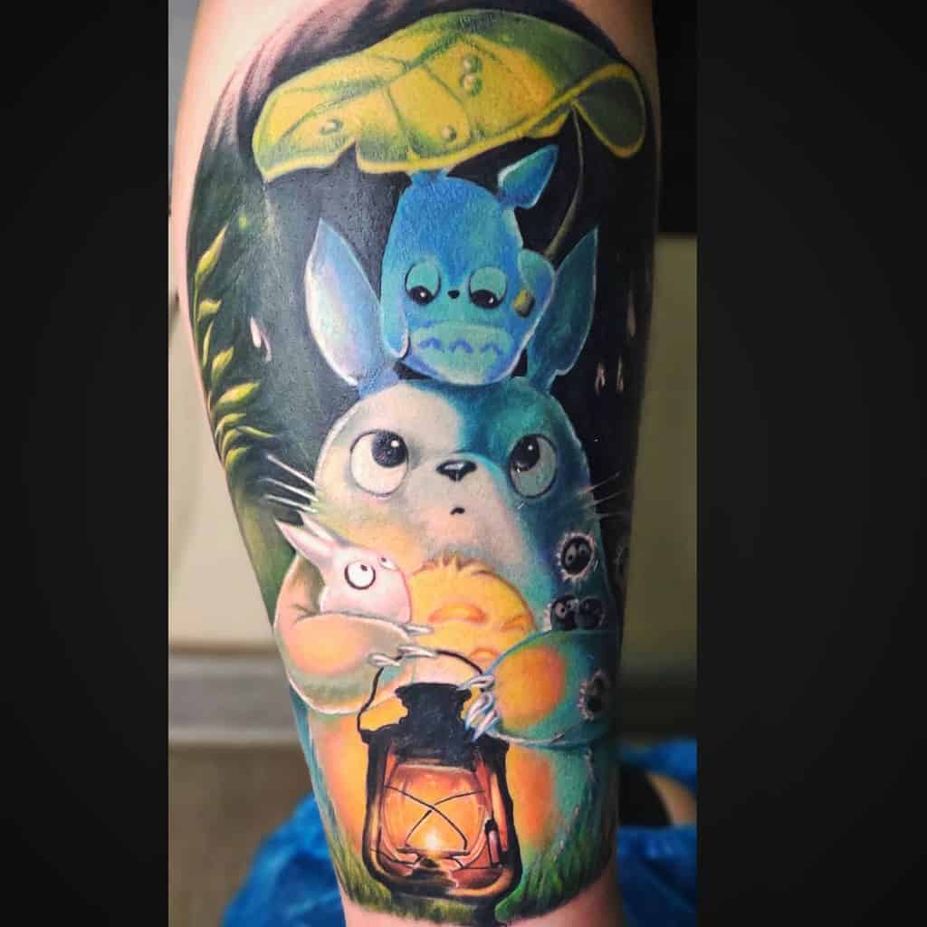 Vibrant Totoro tattoo featuring Totoro characters with a glowing lantern and green leaf, creating a magical night scene