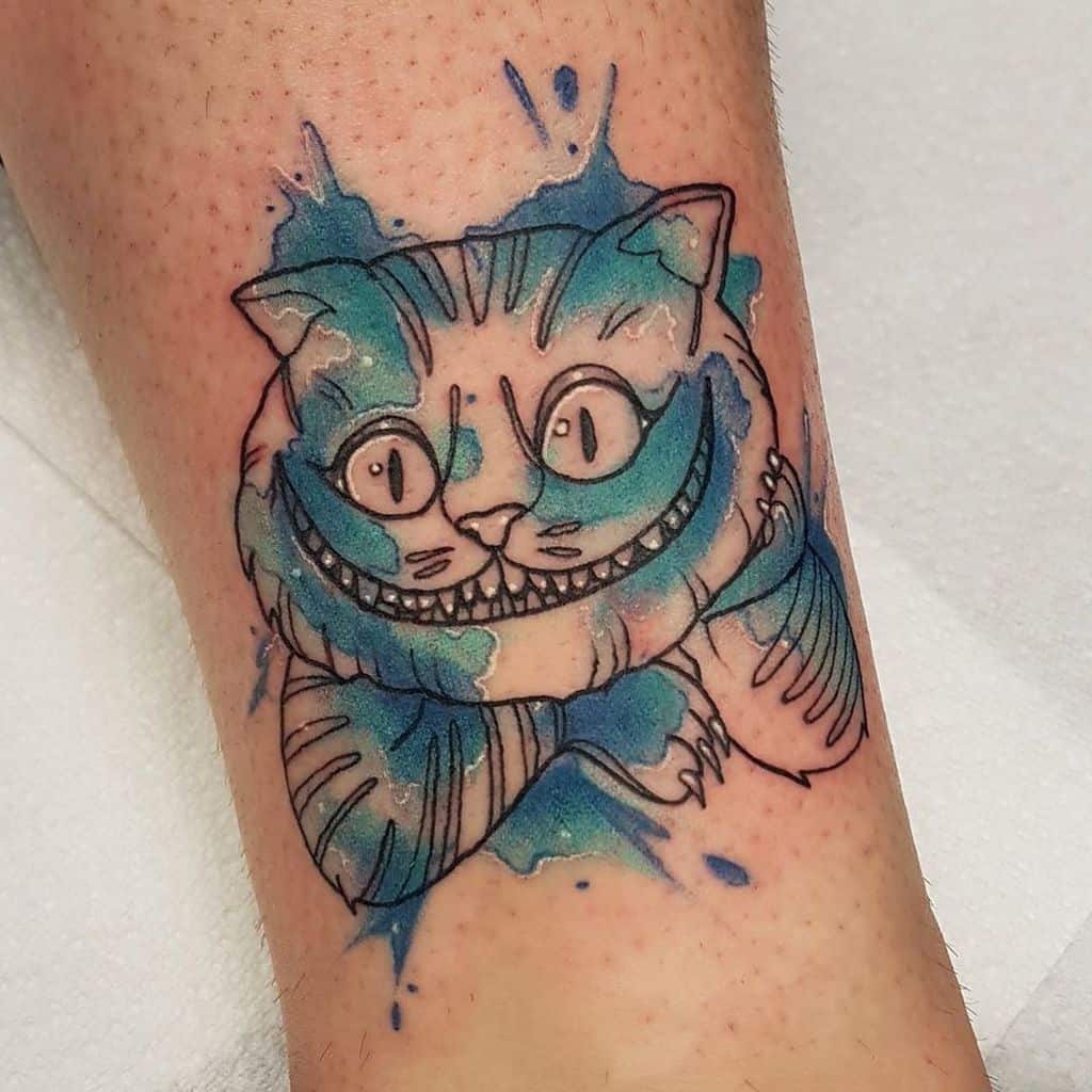 A colorful tattoo of the Cheshire Cat from Alice in Wonderland, with vibrant blue watercolor splashes and outlined details