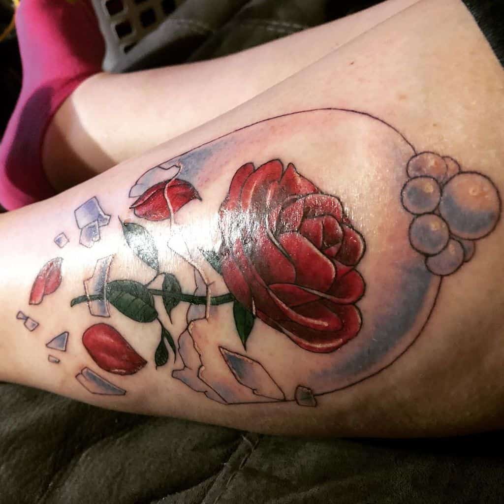 Leg tattoo featuring a red rose in a broken glass dome with scattered petals