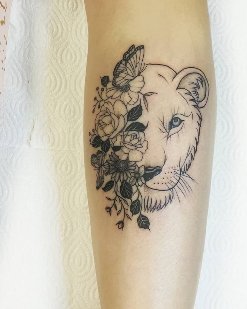 Elegant lioness tattoo on the leg, featuring a half-face design with intricate floral details, a butterfly, and fine linework for a delicate look.