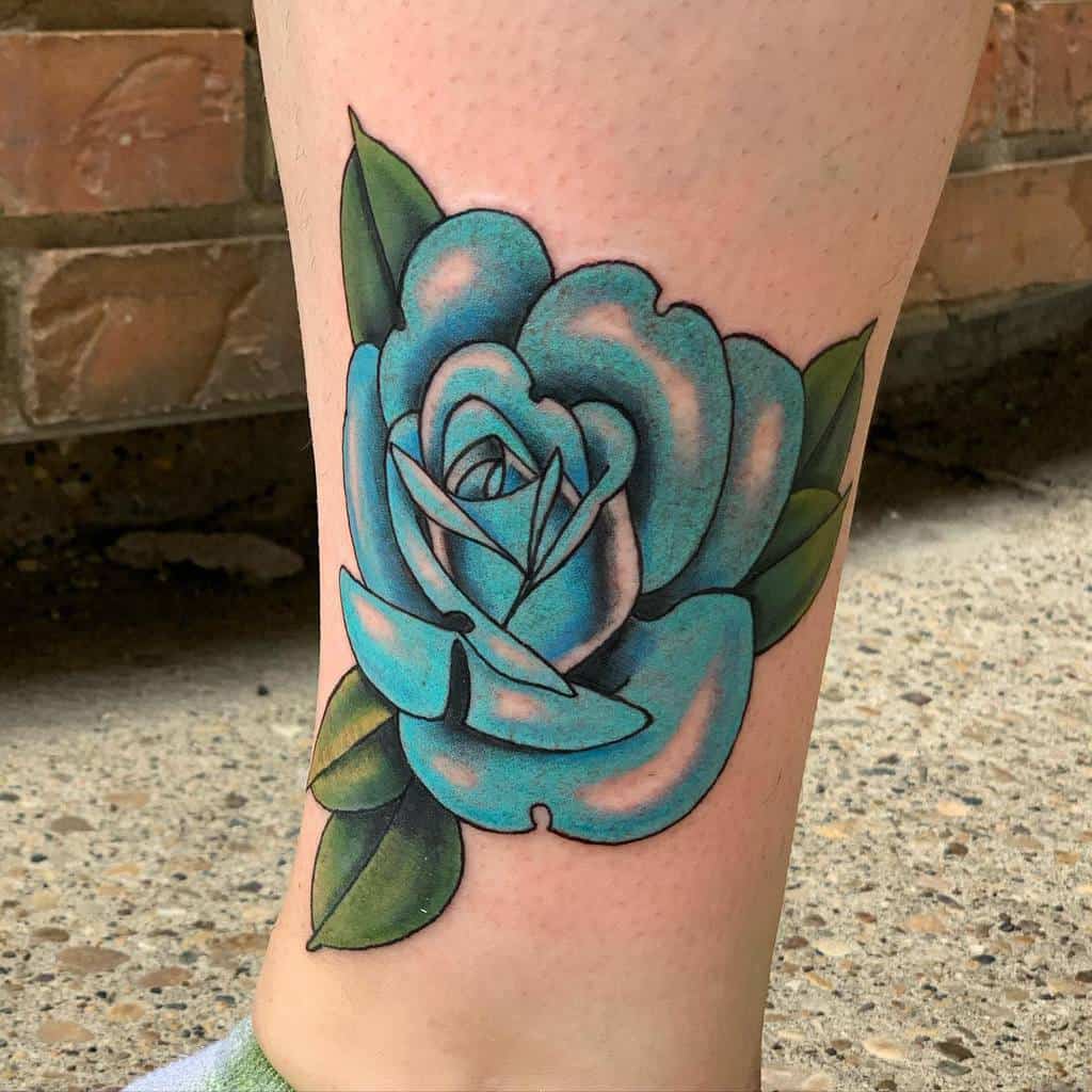 A stunning tattoo of a vibrant blue rose, accentuated by lush green leaves, adorns the person's leg