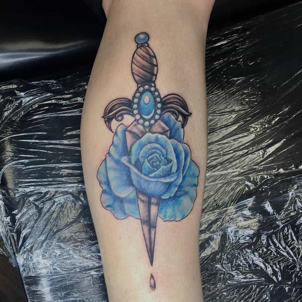 A tattoo of a sharp dagger piercing through a delicate blue rose, with a single teardrop elegantly falling below