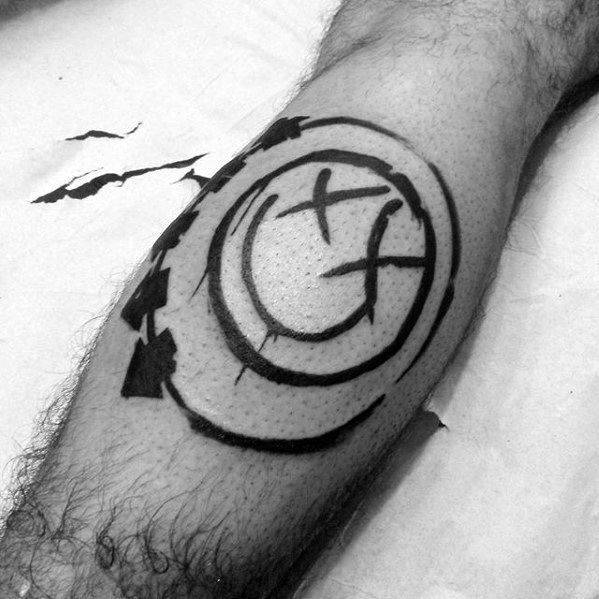 Black and gray tattoo of the Blink-182 smiley face logo with bold strokes and abstract, shattered effects, placed on the forearm.