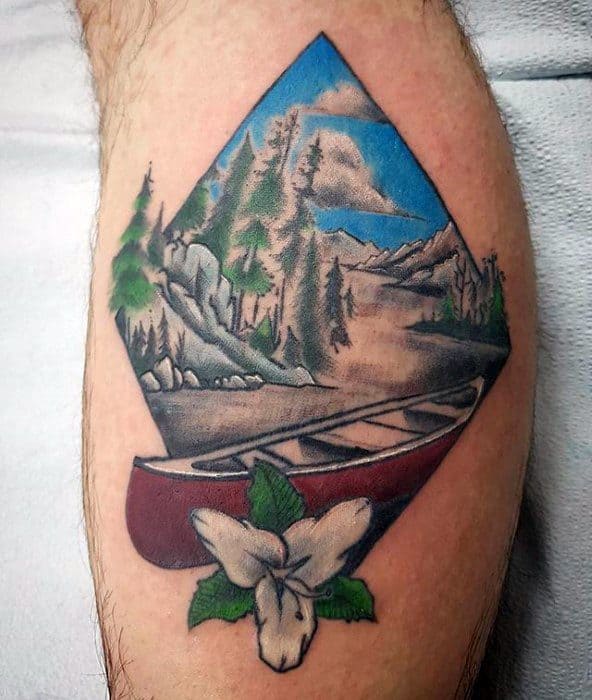Alt text: Colorful tattoo featuring a canoe on a scenic river surrounded by mountains and trees, with a white flower at the base, framed in a diamond shape.