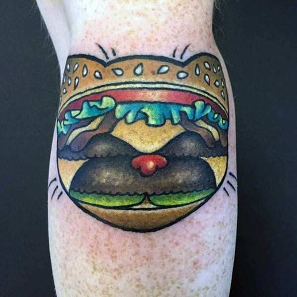 Tattoo of a cat's face inside a cheeseburger bun, with lettuce and tomato details
