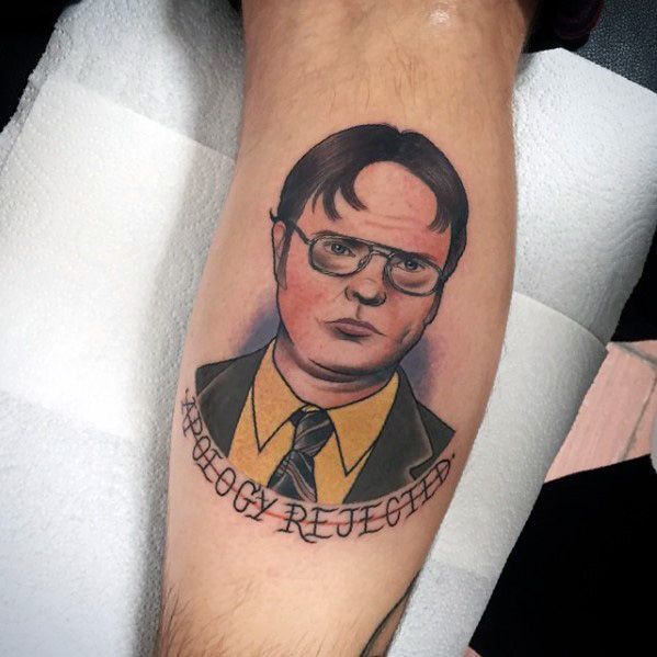Tattoo of Dwight Schrute with a serious expression, wearing his signature glasses and suit, with "APOLOGY REJECTED" written below in bold font.