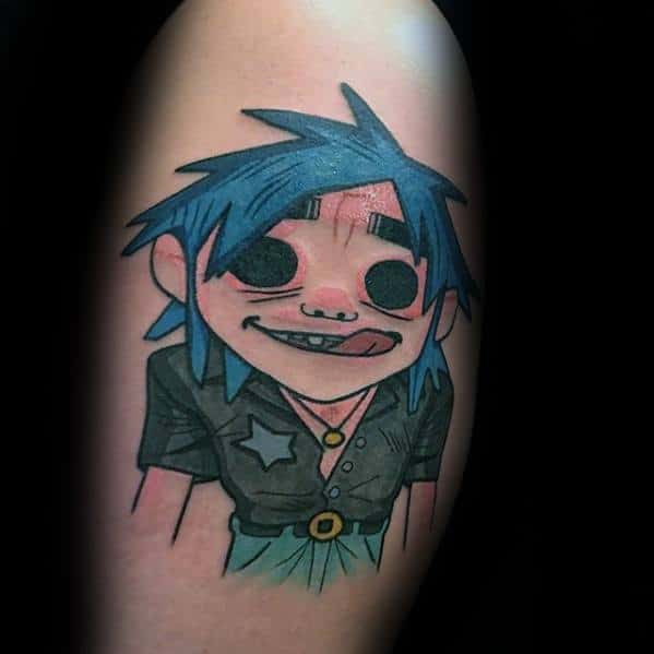 Color tattoo of 2D from Gorillaz with blue spiky hair, wide eyes, tongue out, wearing a black shirt with a star and gold belt detail.
