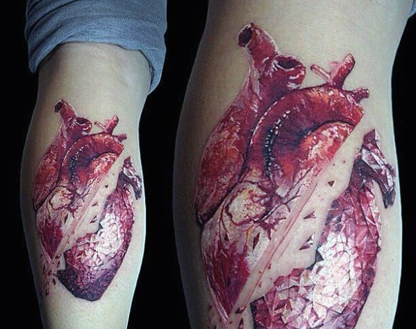 Hyper-realistic tattoo of an anatomical heart, partially shattered like glass, with a sharp-edged fragment cutting through it